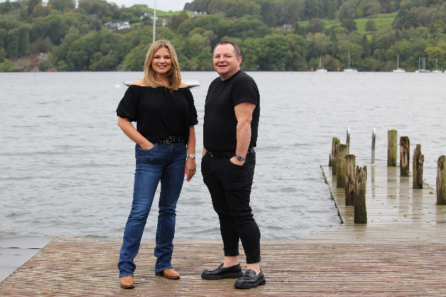 A man and woman smiling at the camera in front of a lake