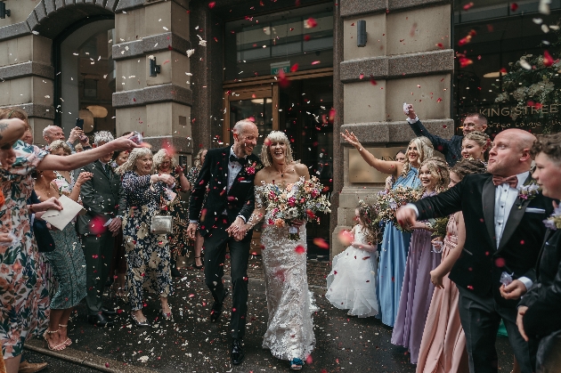 A bride and groom smiling as their friends throw confetti over them