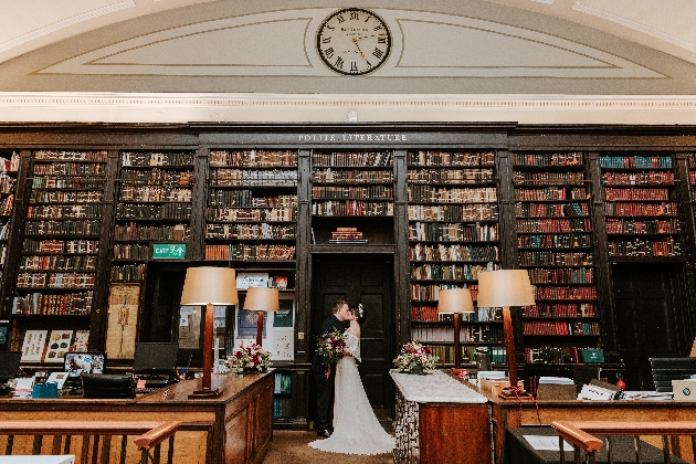 A bride and groom kissing under a large bookcase