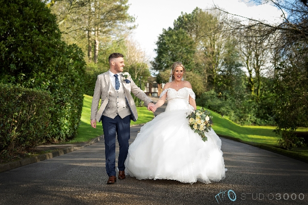 A bride and groom walking hand-in-hand down a driveway