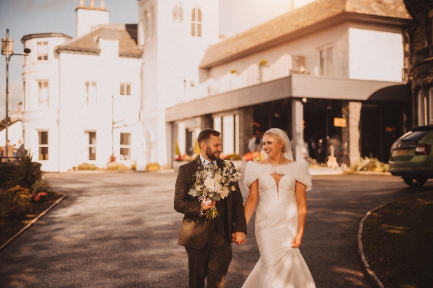 A bride and groom walking hand-in-hand in front of a white building