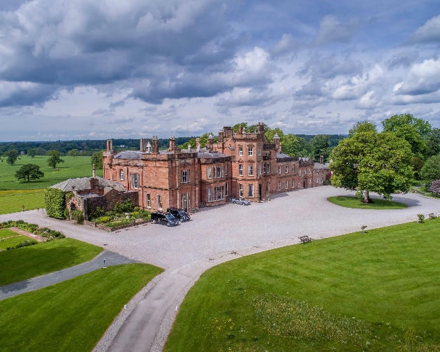 The exterior of a large red manor house surrounded by grounds