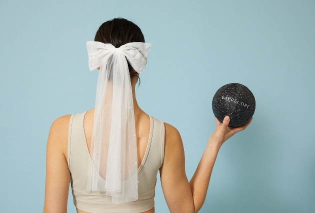 A woman with her back to the camera wearing a veil and holding a black ball that says Barrecore 