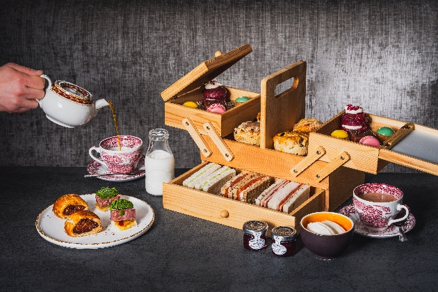 A wooden picnic hamper full of sandwiches, cakes and scones