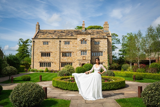 A bride standing outside of a large brick building surrounded by manicured gardens