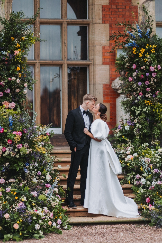 A bride and groom kissing while surrounded by flowers