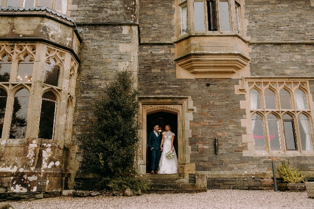 A bride and groom standing in a doorway of a grand brick building