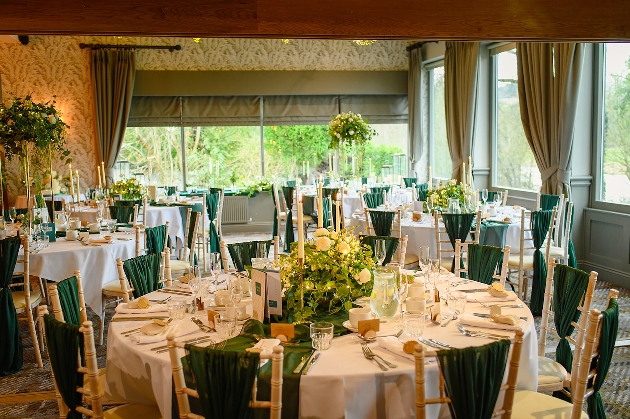 A room decorated with round tables, flowers and green chair sashes