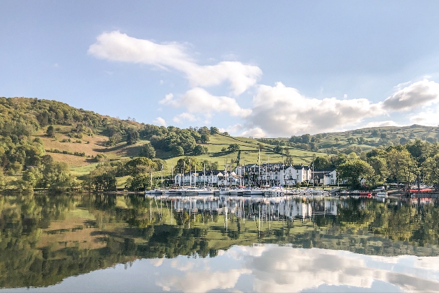 A large white building next to a lake with hills behind it