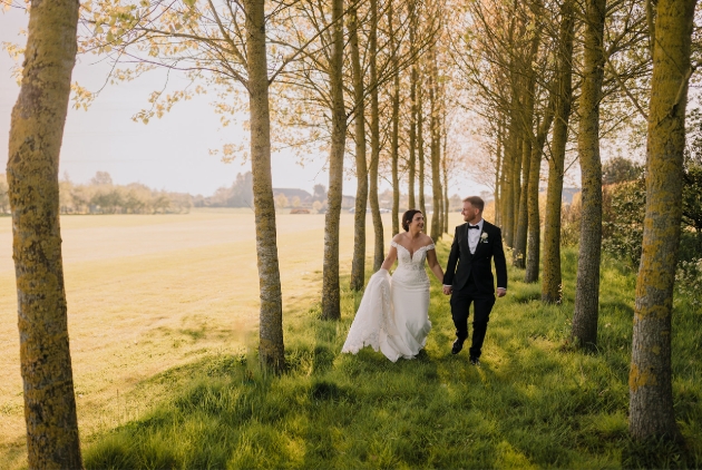 A bride adn groom walking hand-in-hand in a field