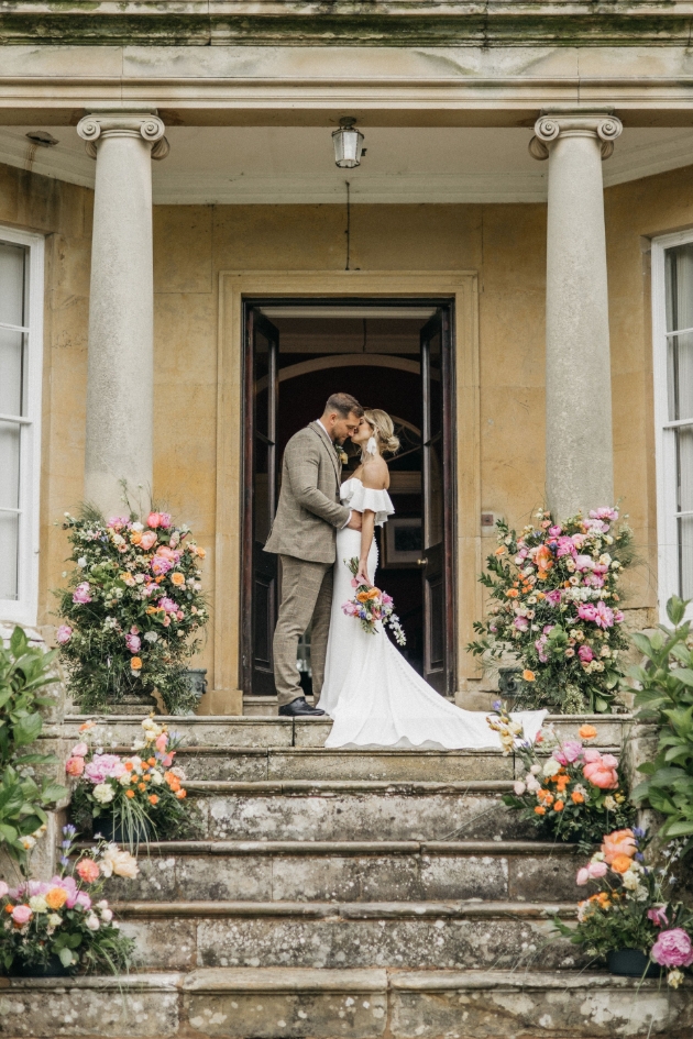 A bride and groom standing on steps surrounded by flowers